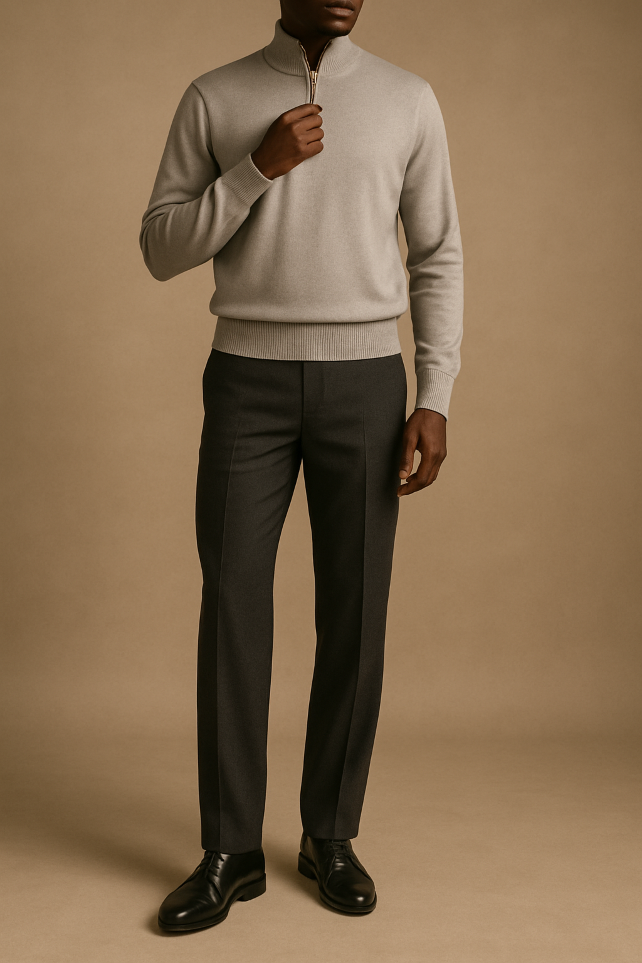 Man wearing a light gray sweater and dark gray pants against a beige background